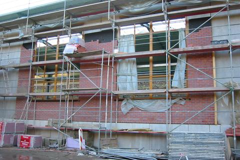 Fassadenansicht mit eingesetzten Fensterrahmen. Zum Schutz der Holzfenster werden diese mittels Folie geschützt.