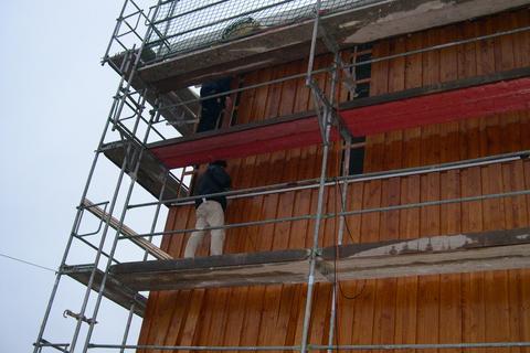 An vier Flächen der Hallenfassade wird eine großflächige Holzverschalung an die Wand montiert. Direkt an die zur südlichen Giebelwand anliegenden Fläche sind die Arbeiten bereits weit fortgeschritten.