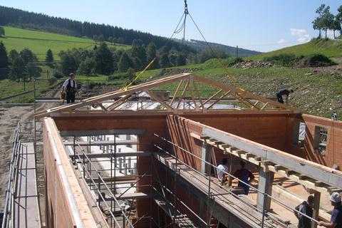 Aufsetzen und Positionieren des ersten Dachbinders auf dem Rohbau des Mehrzweckgebäudes.
