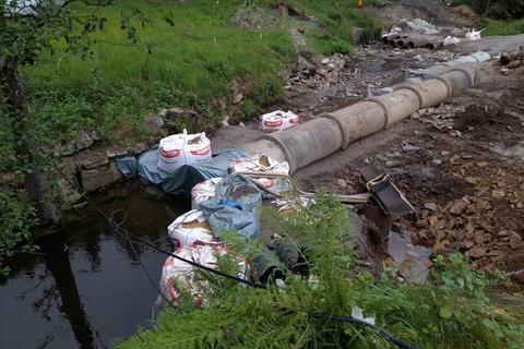 Mit Sandsäcken wird die Wasserhaltung abgedichtet, so dass das Laufwasser durch die beiden Rohre fließen kann.