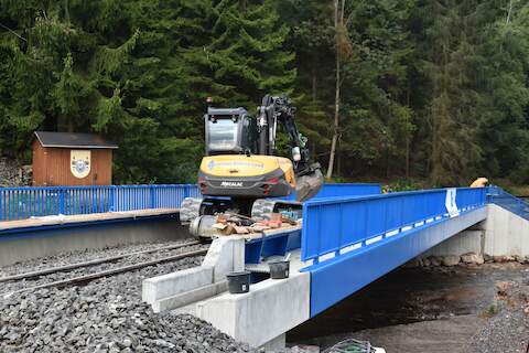 Der Mehrwegebagger befährt bereits das montierte Gleis auf der Brücke.